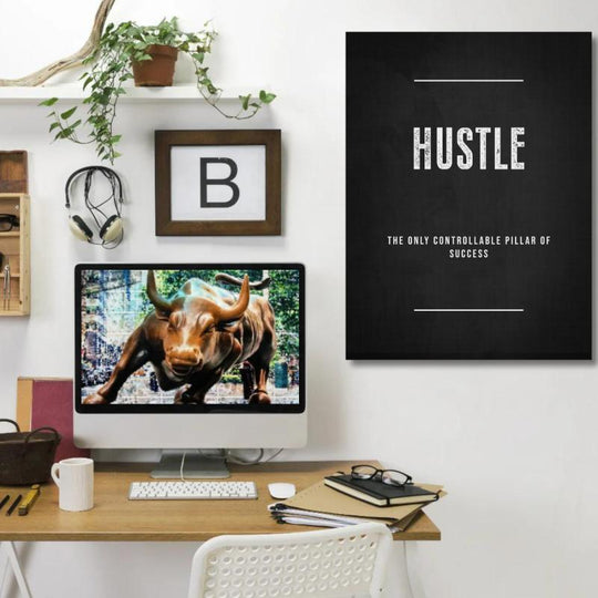 HUSTLE motivational wall art above a wooden desk with a bull figure and green indoor plant.