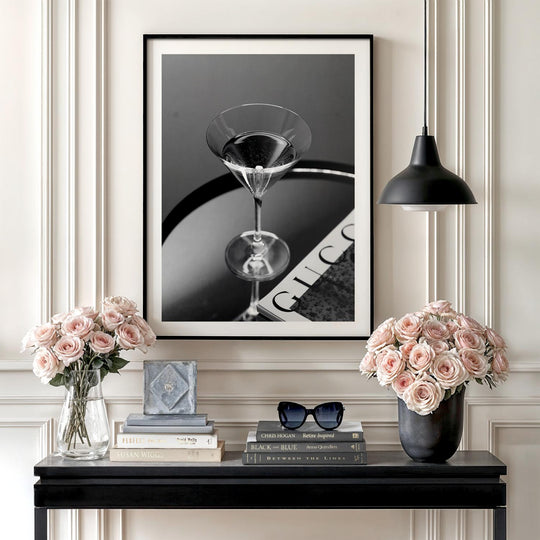 Modern wall art with a black and white photo of a martini glass on a magazine above a console with roses.