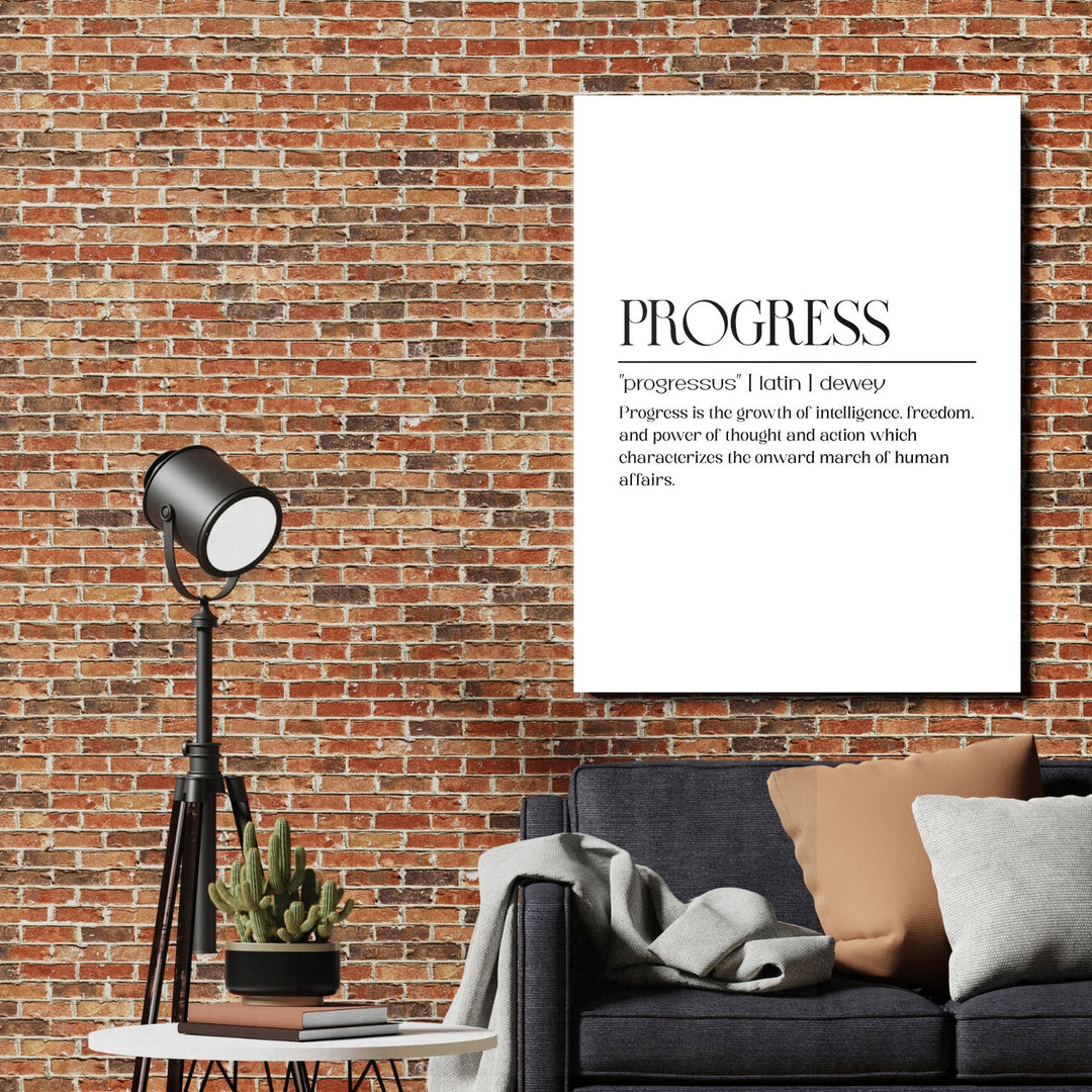 Motivational canvas print with the word PROGRESS on a brick wall above a sofa and floor lamp