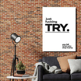 Motivational canvas print “just fucking TRY” on a brick wall in a living room above a sofa and floor lamp