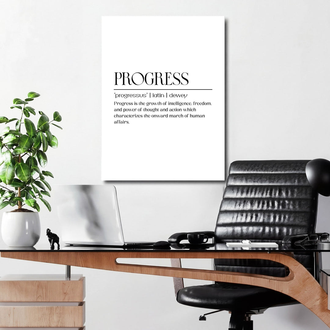 Black-and-white “Progress” motivational canvas print in a modern office above a wooden desk with a laptop and green plant