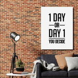 Motivational canvas wall art with the quote “1 DAY OR DAY 1 YOU DECIDE” above a dark gray sofa, lamp and cactus.