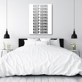 KEEP GOING motivational canvas wall art above a bedroom bed, modern black and white decor in a minimalist interior