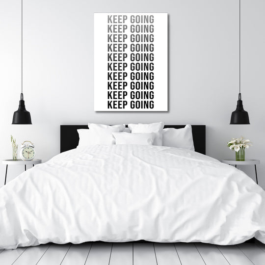 KEEP GOING motivational canvas wall art above a bedroom bed, modern black and white decor in a minimalist interior